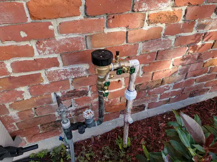 A backflow preventer for a sprinkler system installed beside the original hose valves at a New Orleans home