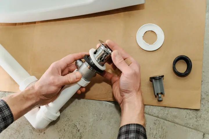 Close-up of a professional plumber's hands rebuilding a sink drain, the kind of work to clarify in the questions to ask a plumber