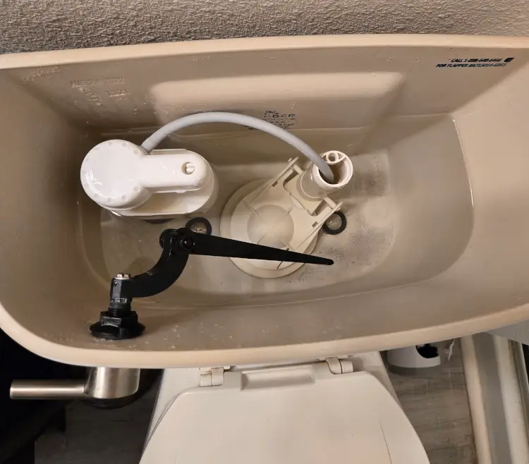 Inside a toilet tank showing the flapper, fill valve, and float that cause a running toilet